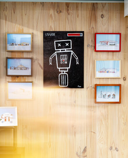8-bit, an acrylic painting of a simple robot, surrounded by my framed prints of WA buildings